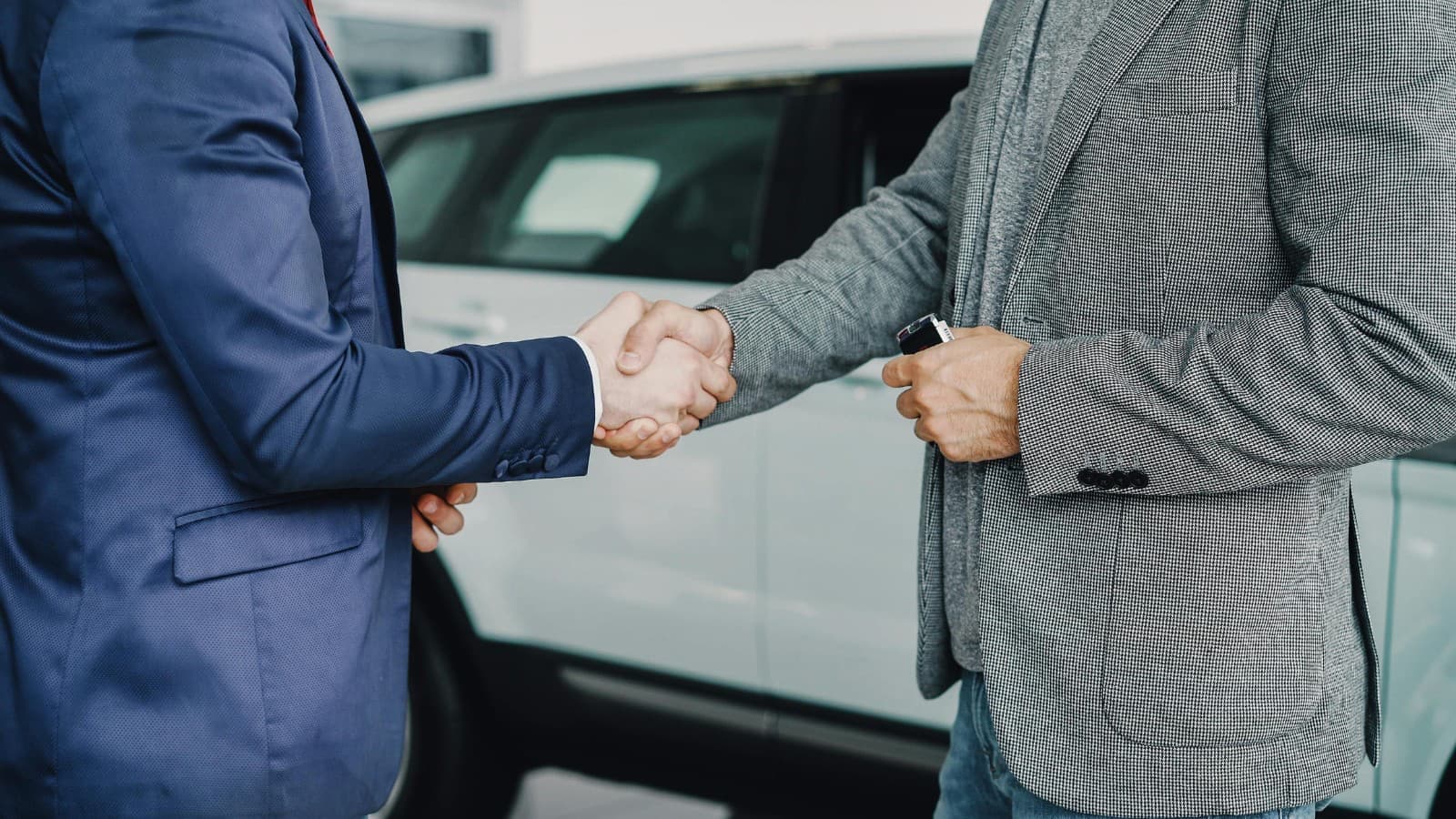 Poignée de main professionnelle entre un courtier automobile et un client devant une berline allemande premium