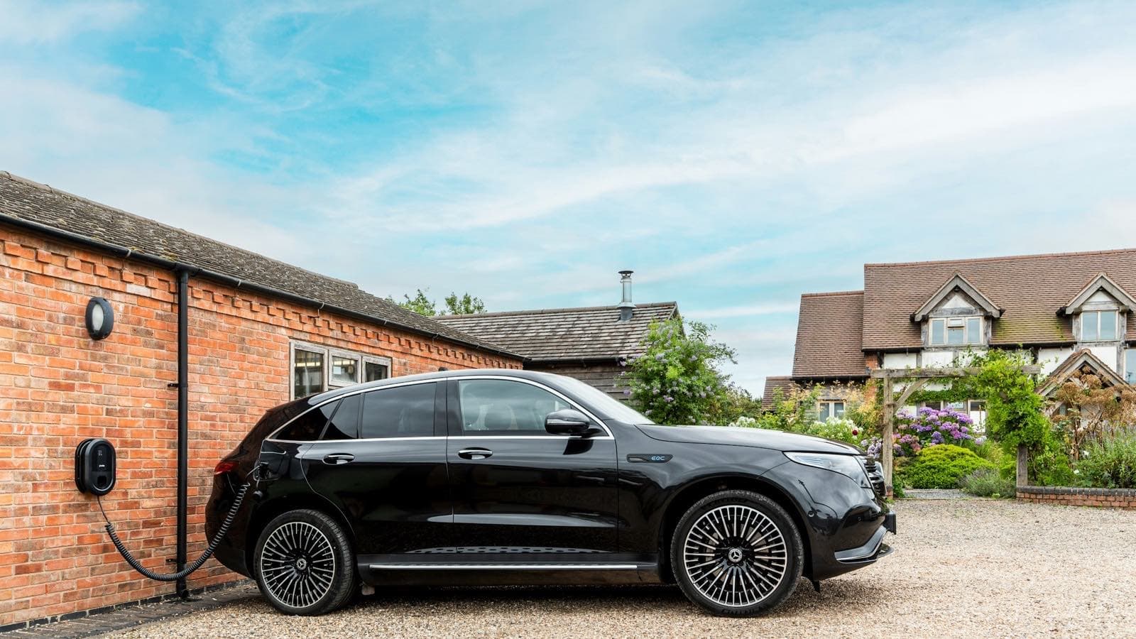 SUV électrique Mercedes EQC noir en charge sur une borne murale devant une maison en brique